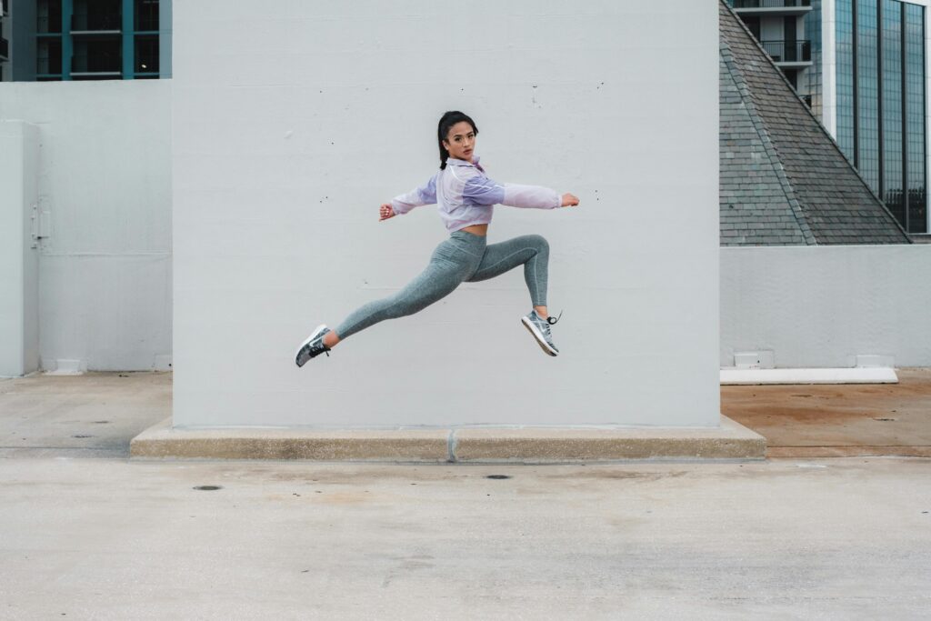 Fit woman in activewear jumps energetically in an urban location, showcasing fitness and agility.